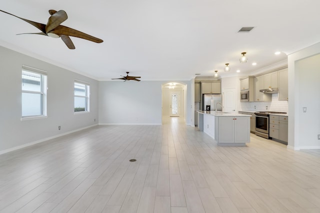 kitchen with appliances with stainless steel finishes, tasteful backsplash, ornamental molding, a kitchen island with sink, and sink