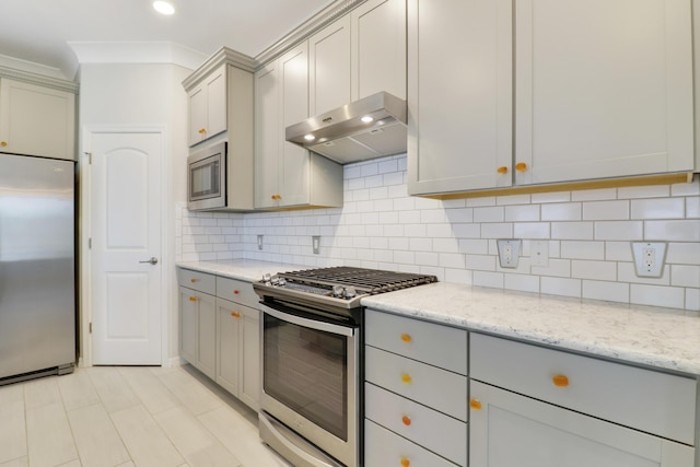 kitchen with gray cabinetry, tasteful backsplash, light stone counters, built in appliances, and ornamental molding