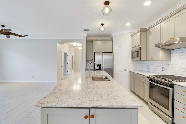 kitchen with backsplash, stainless steel appliances, light stone counters, and a center island with sink