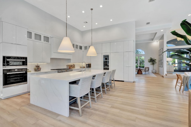 kitchen featuring a high ceiling, white cabinetry, a kitchen island with sink, and light hardwood / wood-style floors