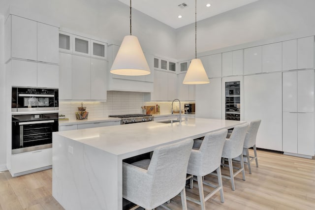 kitchen featuring white cabinetry, sink, light wood-type flooring, and a center island with sink