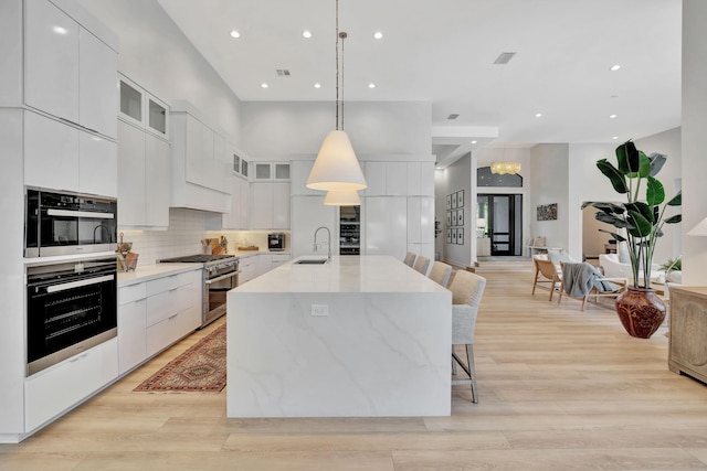 kitchen featuring an island with sink, high end stainless steel range oven, white cabinetry, light hardwood / wood-style floors, and decorative light fixtures