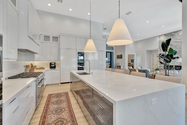 kitchen with white cabinetry, sink, stainless steel range, and decorative light fixtures