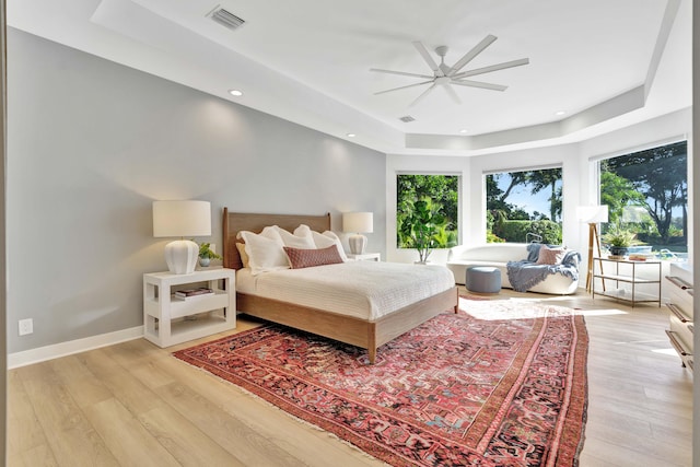 bedroom featuring ceiling fan, a tray ceiling, and light wood-type flooring