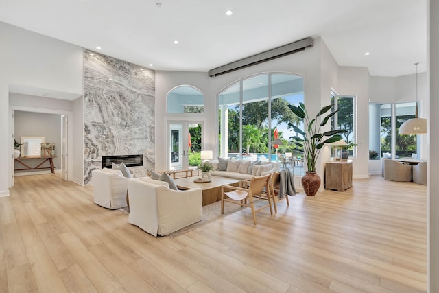 living room with a high end fireplace, a high ceiling, and light hardwood / wood-style flooring