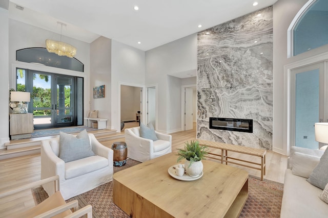 living room with light hardwood / wood-style floors, a notable chandelier, a premium fireplace, and a high ceiling