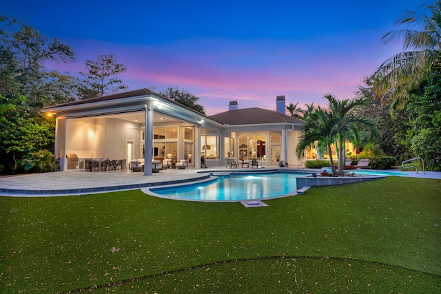 pool at dusk featuring a patio area and a lawn