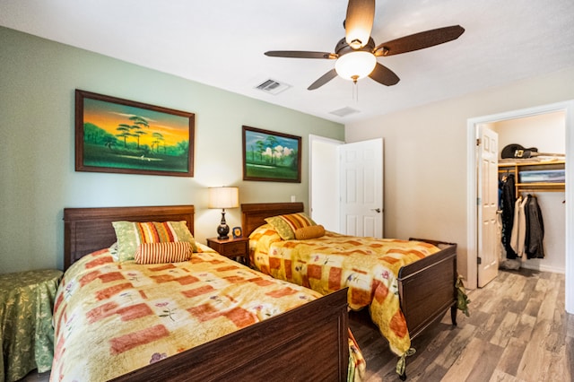 bedroom featuring a walk in closet, a closet, wood-type flooring, and ceiling fan