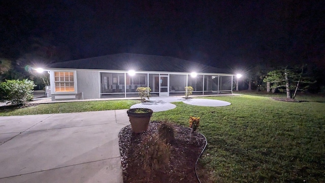 back house at twilight with a lawn and a sunroom