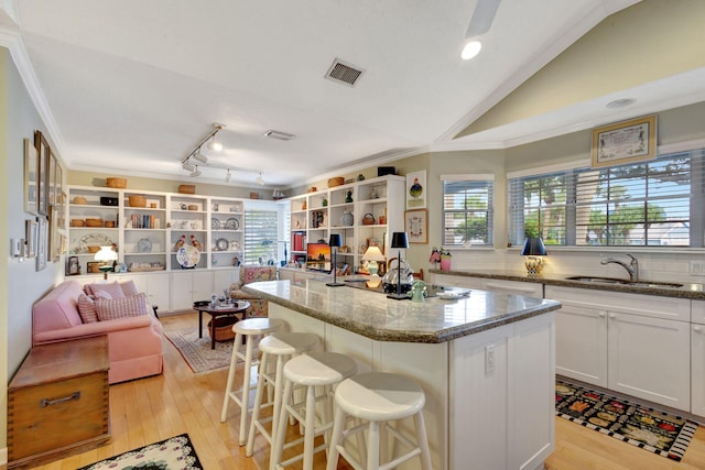 kitchen with sink, light wood-type flooring, a center island, white cabinetry, and light stone counters