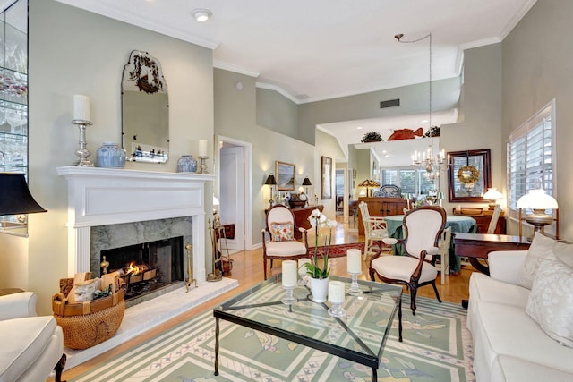 living room with an inviting chandelier, ornamental molding, a high ceiling, a fireplace, and light hardwood / wood-style floors