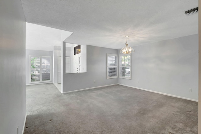 spare room featuring a textured ceiling, light carpet, and a notable chandelier