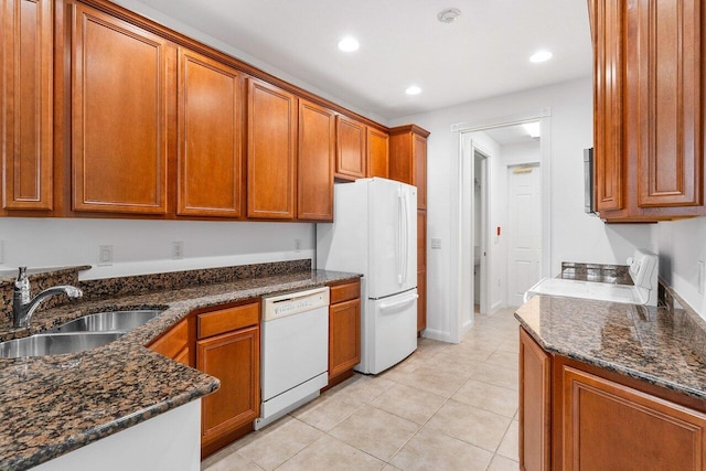 kitchen featuring light tile patterned floors, white appliances, dark stone counters, and sink