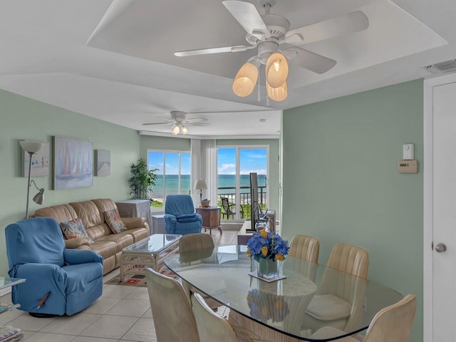 dining room featuring a raised ceiling, a water view, light tile patterned floors, and ceiling fan