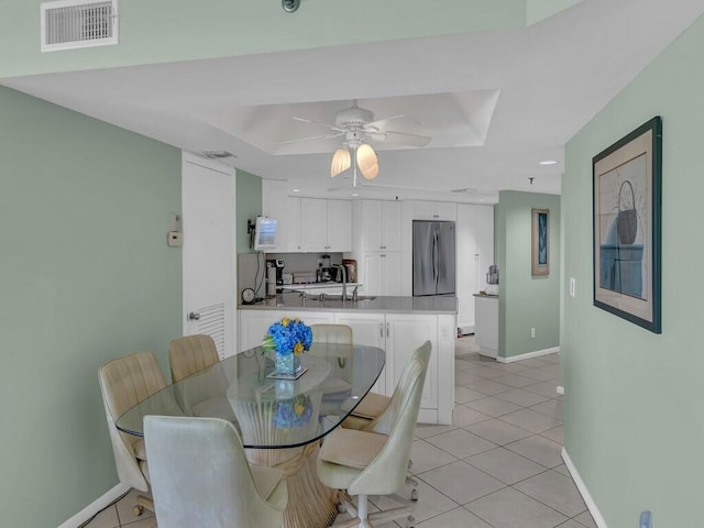 tiled dining room with ceiling fan, a raised ceiling, and sink