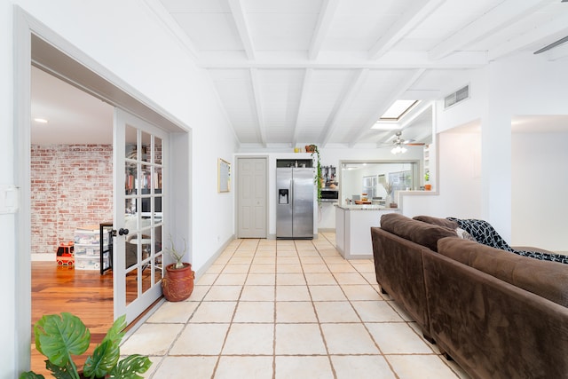 living room featuring ceiling fan, vaulted ceiling with skylight, and light tile patterned floors