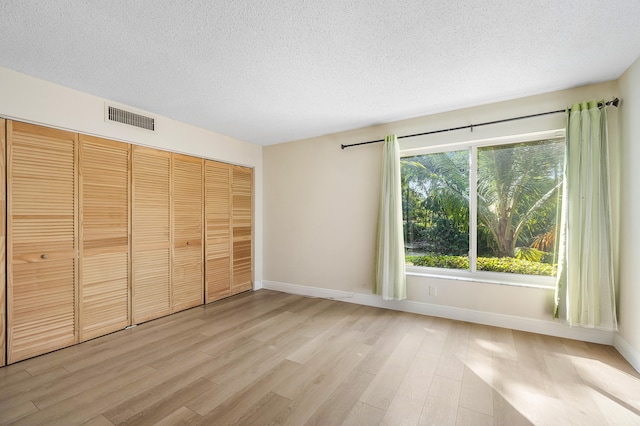 unfurnished bedroom with a textured ceiling, a closet, and light hardwood / wood-style floors