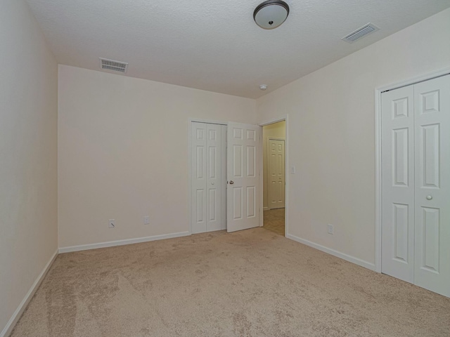 unfurnished bedroom featuring light colored carpet and multiple closets