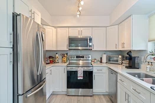 kitchen featuring white cabinets, decorative backsplash, appliances with stainless steel finishes, light hardwood / wood-style flooring, and sink