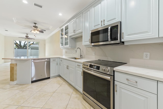 kitchen with appliances with stainless steel finishes, sink, kitchen peninsula, white cabinets, and ornamental molding