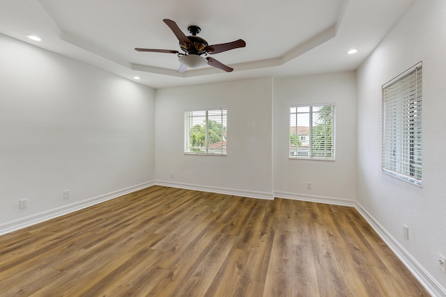 empty room with hardwood / wood-style floors, a tray ceiling, and ceiling fan