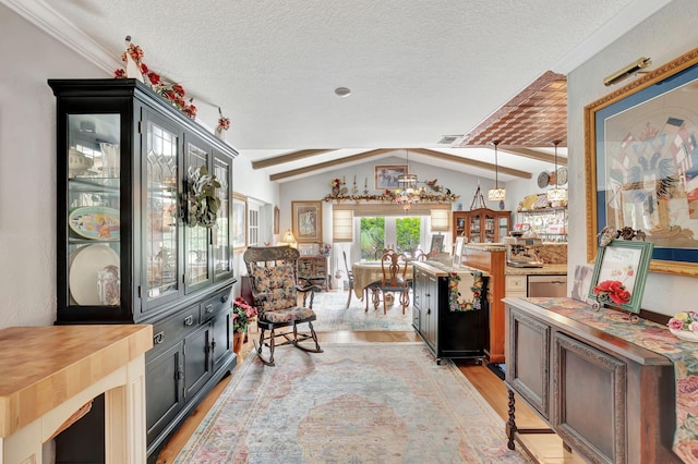 interior space with vaulted ceiling with beams, a textured ceiling, decorative light fixtures, and light hardwood / wood-style floors