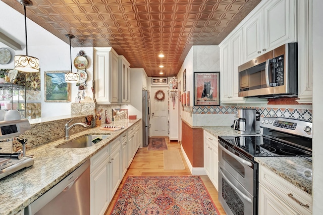 kitchen with light hardwood / wood-style flooring, sink, pendant lighting, appliances with stainless steel finishes, and light stone counters