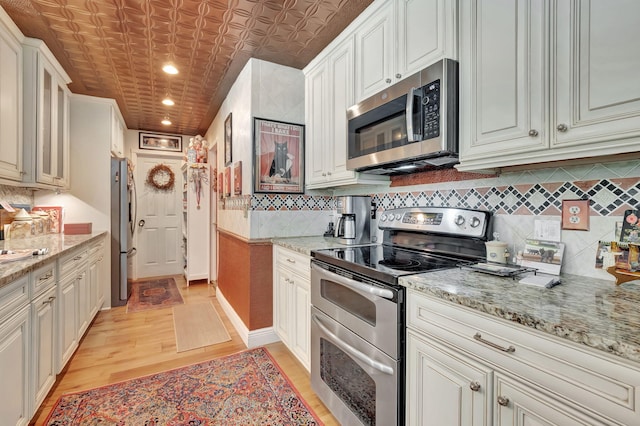 kitchen with light hardwood / wood-style flooring, white cabinetry, light stone countertops, and stainless steel appliances