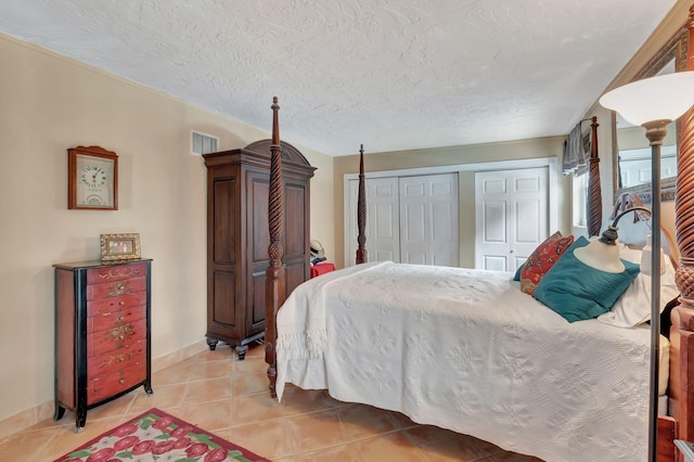 tiled bedroom with a textured ceiling and multiple closets