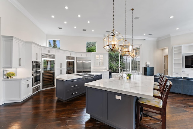 kitchen featuring a large island with sink, white cabinetry, stainless steel appliances, and decorative light fixtures