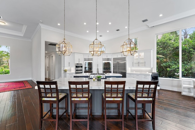 kitchen featuring a large island with sink, white cabinetry, hanging light fixtures, and appliances with stainless steel finishes