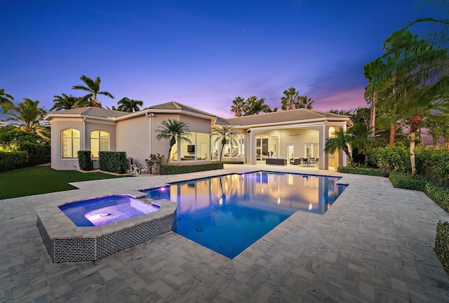 pool at dusk featuring an in ground hot tub, ceiling fan, and a patio