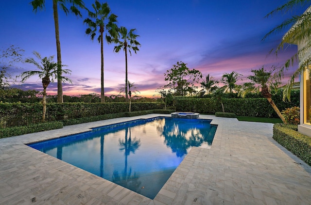 pool at dusk featuring an in ground hot tub