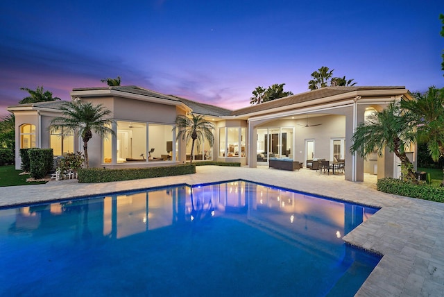 pool at dusk featuring outdoor lounge area, a patio area, and ceiling fan