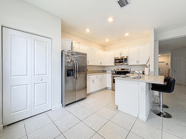 kitchen featuring stainless steel appliances, white cabinets, kitchen peninsula, light tile patterned floors, and a kitchen breakfast bar