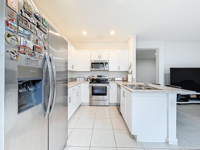 kitchen featuring kitchen peninsula, sink, light tile patterned floors, white cabinetry, and appliances with stainless steel finishes