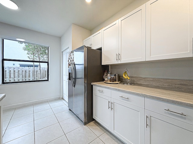 kitchen with white cabinets, light tile patterned flooring, and stainless steel fridge