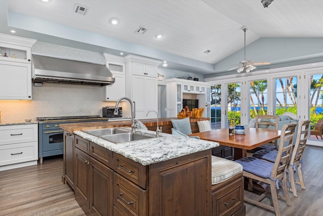 kitchen with high end stainless steel range oven, sink, wall chimney range hood, white cabinets, and lofted ceiling