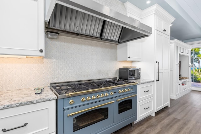 kitchen featuring light stone countertops, wall chimney exhaust hood, double oven range, and white cabinetry