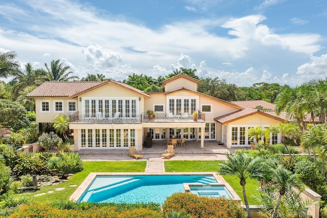 back of house featuring a lawn, a swimming pool with hot tub, french doors, a patio area, and a balcony