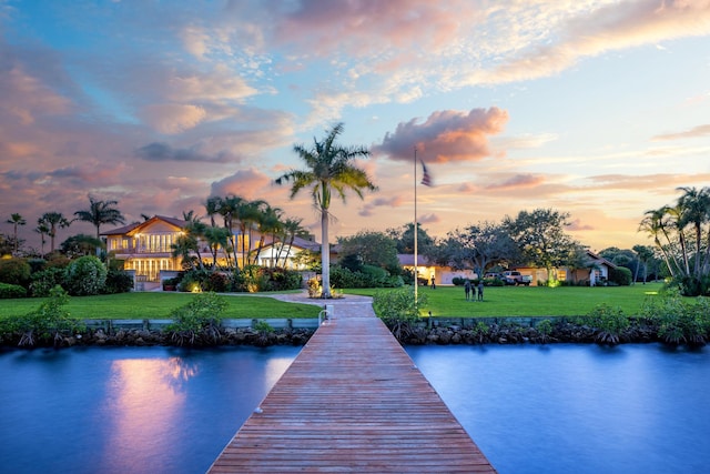 view of dock with a lawn and a water view