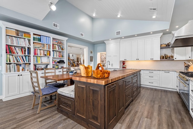 kitchen featuring a center island with sink, butcher block countertops, white cabinets, dark brown cabinets, and range with two ovens