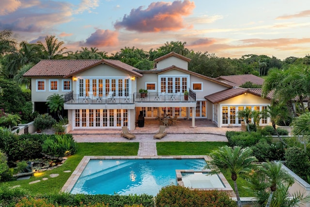 back house at dusk featuring a patio area, french doors, a balcony, and a swimming pool with hot tub