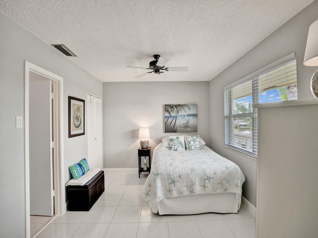 bedroom featuring ceiling fan, light tile patterned flooring, a textured ceiling, and a closet