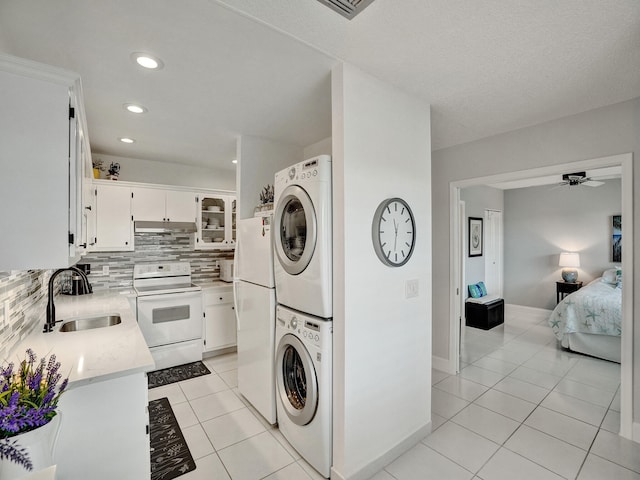 laundry room with light tile patterned floors, stacked washer and dryer, ceiling fan, and sink