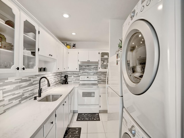 kitchen with white cabinetry, sink, stacked washing maching and dryer, white appliances, and light tile patterned flooring