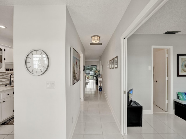 hallway featuring light tile patterned floors, a textured ceiling, and sink