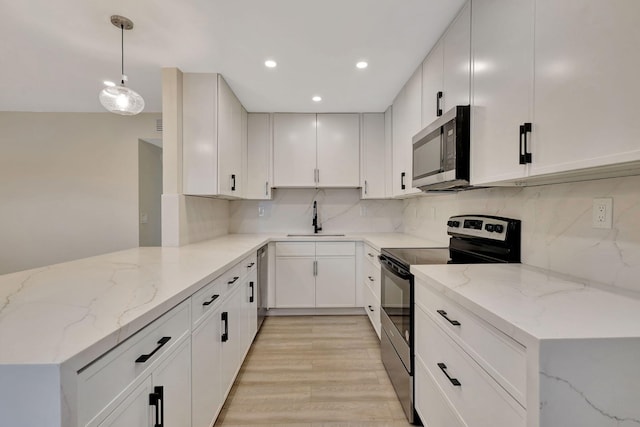 kitchen featuring a peninsula, light stone counters, stainless steel appliances, and a sink