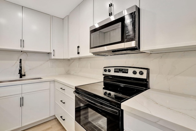 kitchen with black / electric stove, white cabinetry, stainless steel microwave, and a sink