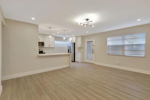 unfurnished living room featuring an inviting chandelier, recessed lighting, light wood-style flooring, and baseboards